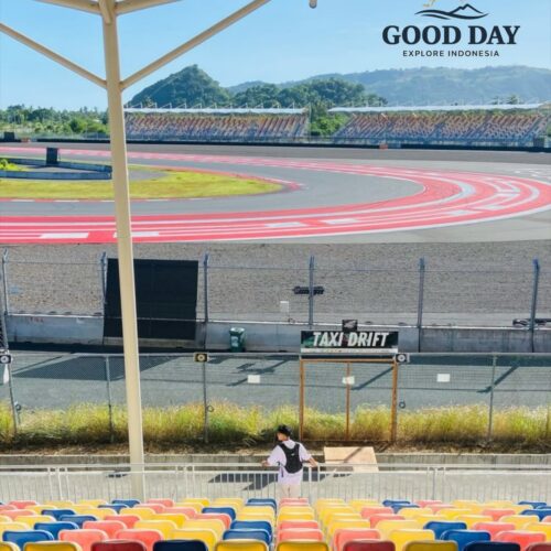 Visitor enjoying the grandstand view at Pertamina Mandalika International Circuit in Lombok, Indonesia, overlooking a famous sweeping corner of the MotoGP race track with colorful spectator seats and scenic hills in the background.