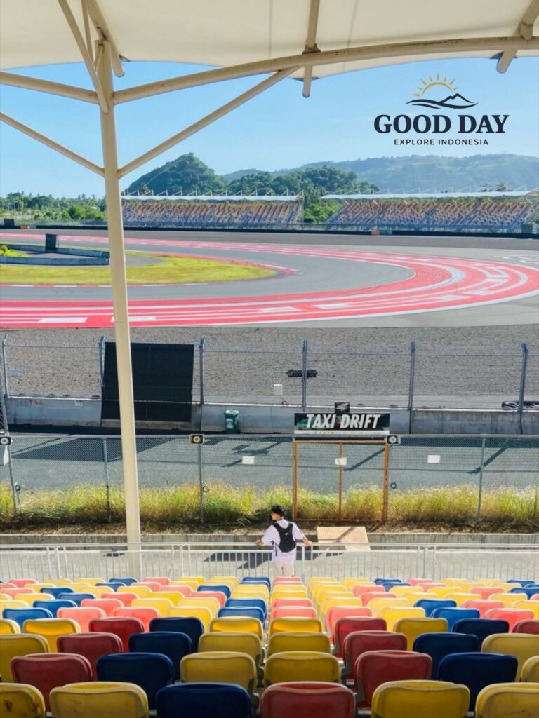 Visitor enjoying the grandstand view at Pertamina Mandalika International Circuit in Lombok, Indonesia, overlooking a famous sweeping corner of the MotoGP race track with colorful spectator seats and scenic hills in the background.
