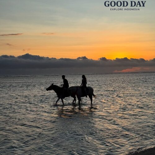 Horse riding at sunset in Gili Islands, Lombok, Indonesia, with two riders on horseback walking through shallow seawater along the beach as the golden sunset reflects across the ocean.