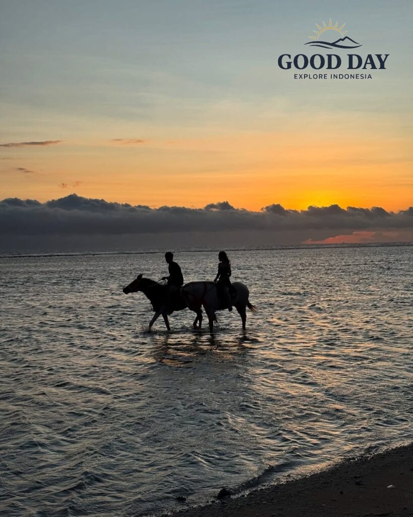 Horse riding at sunset in Gili Islands, Lombok, Indonesia, with two riders on horseback walking through shallow seawater along the beach as the golden sunset reflects across the ocean.