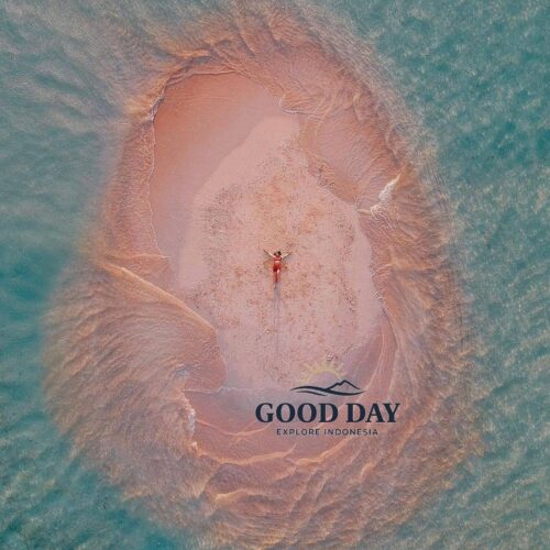 A breathtaking aerial view of Gili Pasir Lombok, featuring a tiny pink-tinted sandbar emerging from crystal-clear turquoise waters. A traveler lies at the center of the sandbank, surrounded by naturally sculpted tidal patterns, showcasing one of Lombok’s most unique and photogenic hidden island destinations.
