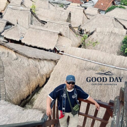 Visitor standing on a traditional wooden viewing platform overlooking the iconic thatched-roof houses of Sade Traditional Village in Lombok, Indonesia. The Sasak cultural village showcases authentic indigenous architecture, local heritage, and rural village life.