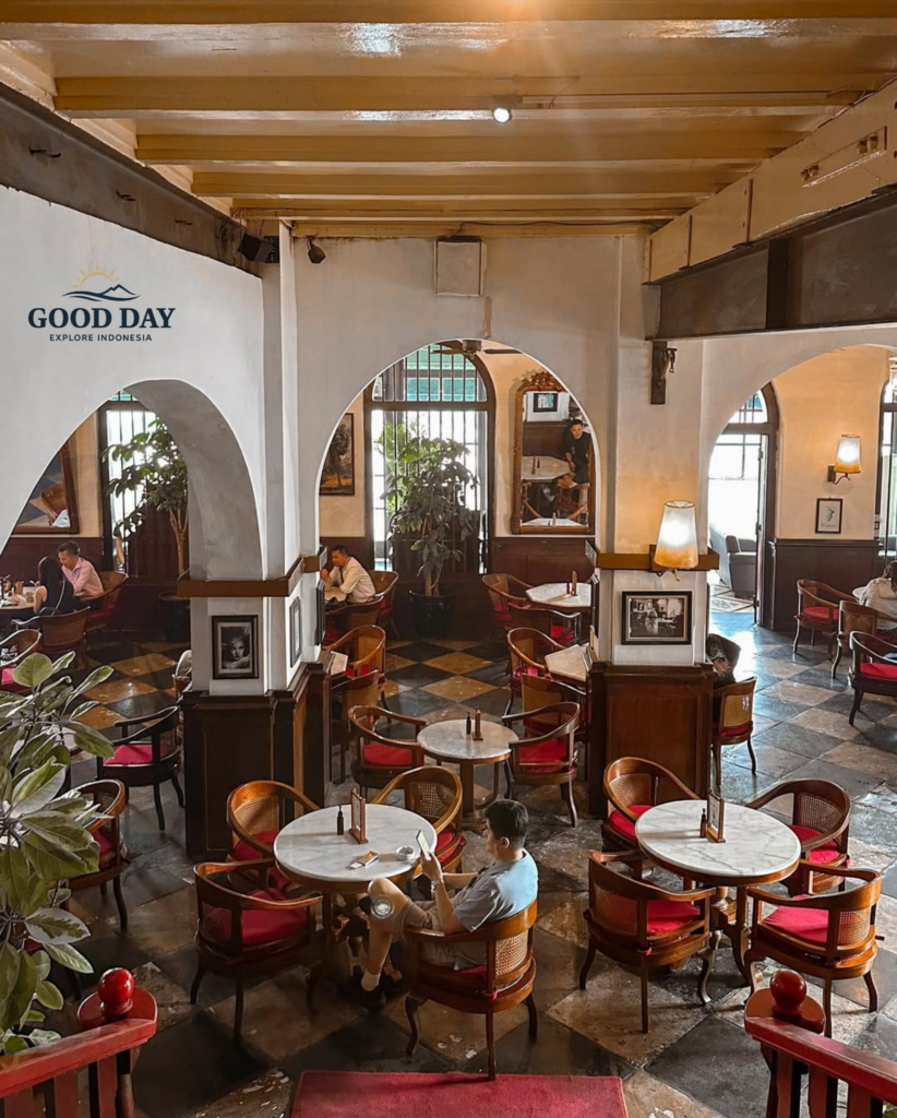 Interior of Café Batavia Jakarta featuring elegant colonial architecture, marble-top tables, vintage wooden furniture, red-upholstered chairs, and arched hallways. Guests relax and dine within one of the most iconic heritage cafés overlooking Kota Tua Jakarta.