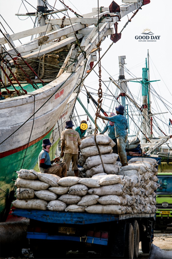 Cargo workers loading and unloading goods at Sunda Kelapa Harbour in Jakarta, Indonesia. Traditional wooden phinisi ships are docked alongside the port while laborers handle sacks of cargo, showcasing the daily maritime trade activities that have sustained Jakarta's historic harbor for centuries.