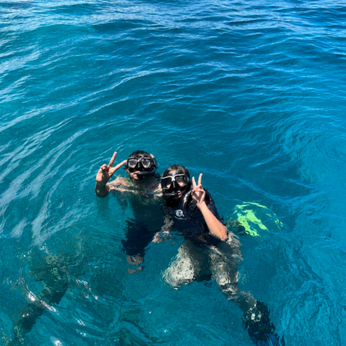 Two snorkelers posing with peace signs in the crystal-clear blue waters of Bunaken Marine Park, Manado, North Sulawesi, Indonesia. Wearing snorkeling masks and fins, they enjoy a tropical marine adventure above Bunaken’s famous coral reef ecosystem.
