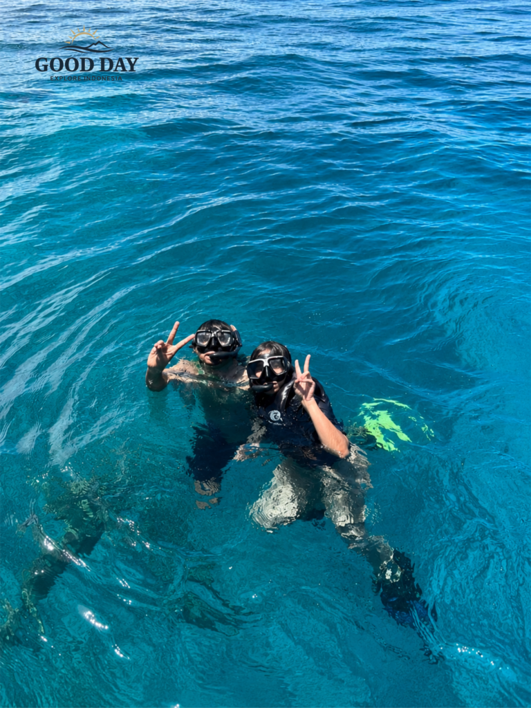 Two snorkelers posing with peace signs in the crystal-clear blue waters of Bunaken Marine Park, Manado, North Sulawesi, Indonesia. Wearing snorkeling masks and fins, they enjoy a tropical marine adventure above Bunaken’s famous coral reef ecosystem.