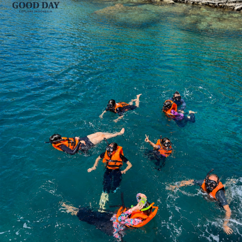 Group of tourists snorkeling in the crystal-clear turquoise waters of Bunaken Marine Park, Manado, North Sulawesi. Visitors wearing life jackets and snorkeling masks enjoy a marine adventure near a rocky coastline surrounded by pristine tropical waters.