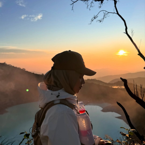 Traveler enjoying sunrise at Sunan Ibu Viewpoint overlooking the turquoise crater lake of Kawah Putih in Ciwidey, Bandung, West Java, Indonesia.