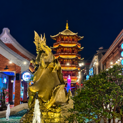 Golden dragon fountain at Pantjoran PIK Jakarta illuminated at night, with a beautifully lit traditional Chinese pagoda in the background. Colorful lights, modern architecture, and vibrant nightlife create a stunning cultural atmosphere in Pantai Indah Kapuk, Jakarta.