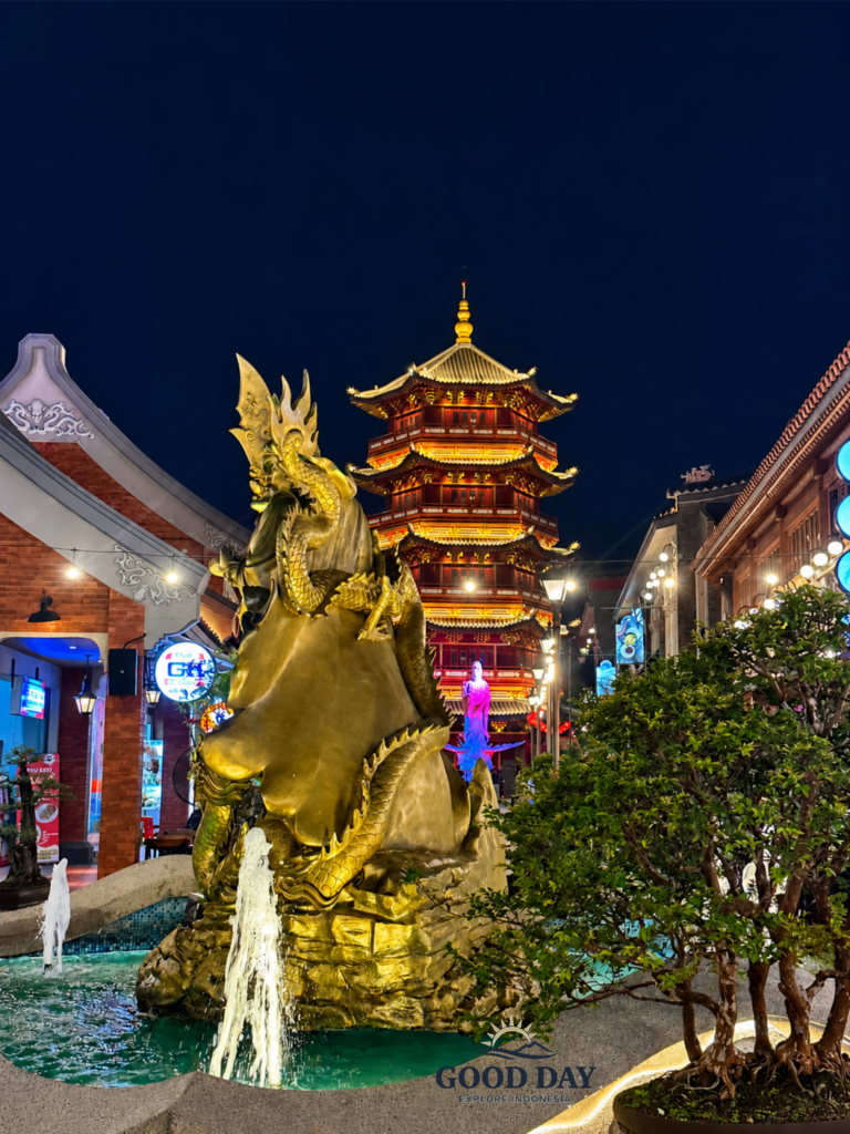 Golden dragon fountain at Pantjoran PIK Jakarta illuminated at night, with a beautifully lit traditional Chinese pagoda in the background. Colorful lights, modern architecture, and vibrant nightlife create a stunning cultural atmosphere in Pantai Indah Kapuk, Jakarta.