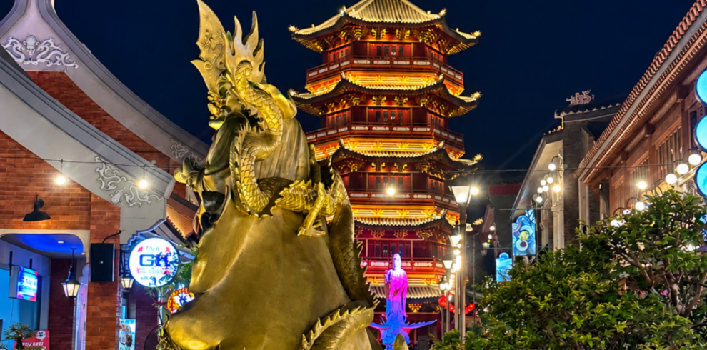 Golden dragon fountain at Pantjoran PIK Jakarta illuminated at night, with a beautifully lit traditional Chinese pagoda in the background. Colorful lights, modern architecture, and vibrant nightlife create a stunning cultural atmosphere in Pantai Indah Kapuk, Jakarta.