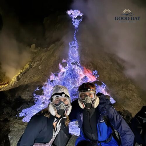 Travelers wearing gas masks pose in front of the famous Blue Fire phenomenon at Kawah Ijen, East Java, Indonesia, surrounded by glowing blue sulfur flames and volcanic smoke at night.