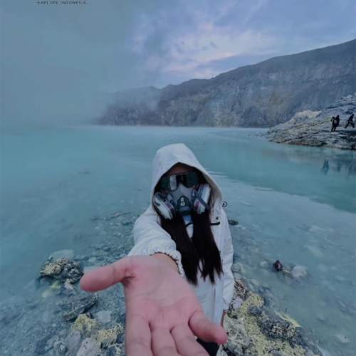 Traveler wearing a gas mask beside the turquoise crater lake of Kawah Ijen, East Java, Indonesia, surrounded by volcanic cliffs, sulfur mist, and the dramatic landscape of one of the world's most unique volcanoes.