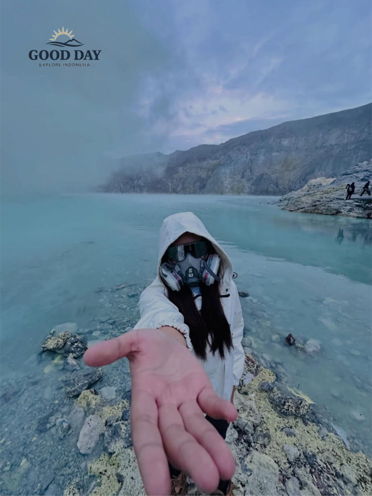 Traveler wearing a gas mask beside the turquoise crater lake of Kawah Ijen, East Java, Indonesia, surrounded by volcanic cliffs, sulfur mist, and the dramatic landscape of one of the world's most unique volcanoes.