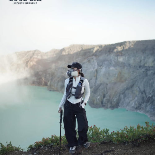 A traveler wearing a gas mask standing on the rim of Kawah Ijen Crater in East Java, Indonesia, overlooking the stunning turquoise acidic lake and dramatic volcanic landscape.