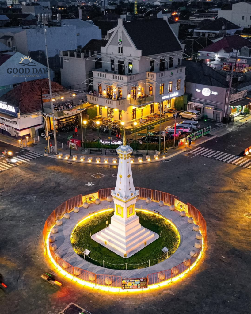 Aerial view of Tugu Yogyakarta at night, featuring the iconic white monument illuminated by golden lights at the center of one of Yogyakarta's most famous landmarks.