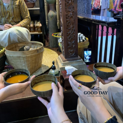 Traditional Javanese jamu tasting experience in Yogyakarta, Indonesia, with visitors holding coconut-shell bowls filled with herbal turmeric drink inside a cozy cultural shop featuring batik textiles, wooden carvings, and authentic Javanese décor.