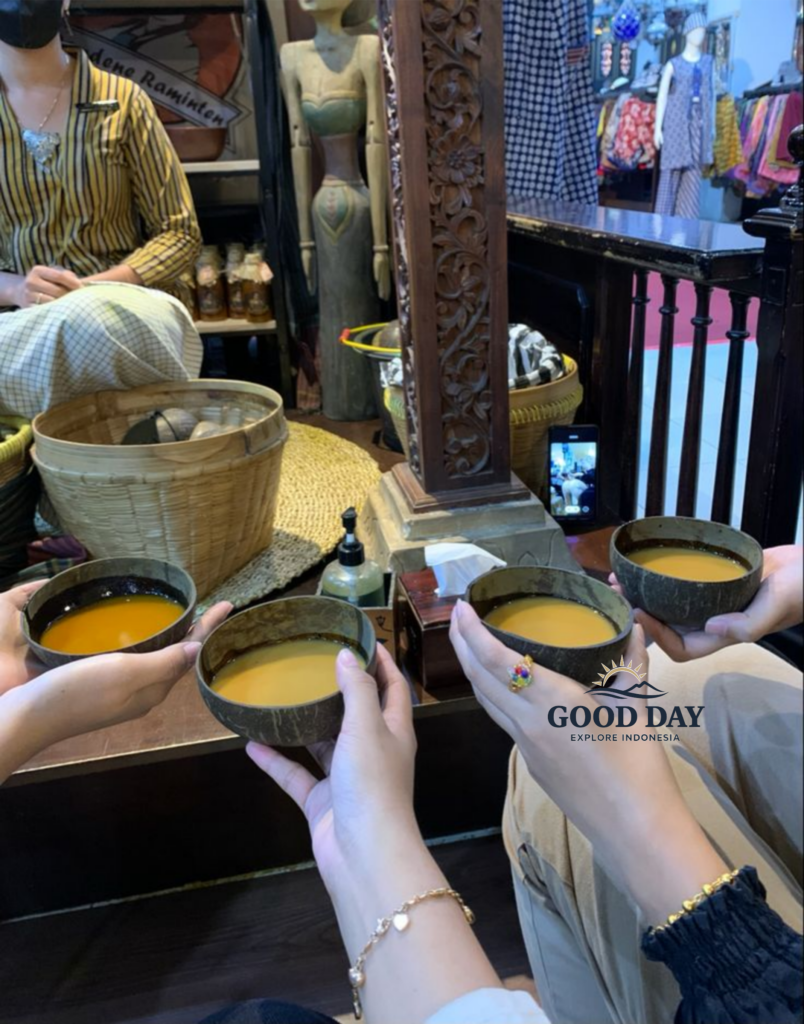 Traditional Javanese jamu tasting experience in Yogyakarta, Indonesia, with visitors holding coconut-shell bowls filled with herbal turmeric drink inside a cozy cultural shop featuring batik textiles, wooden carvings, and authentic Javanese décor.