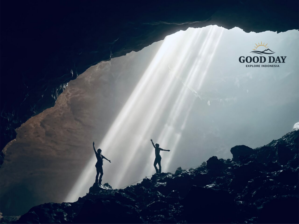 Visitors standing beneath the famous Heaven's Light sunbeams inside Jomblang Cave, Yogyakarta, Indonesia, as sunlight streams through the cave opening and illuminates the vast underground chamber.