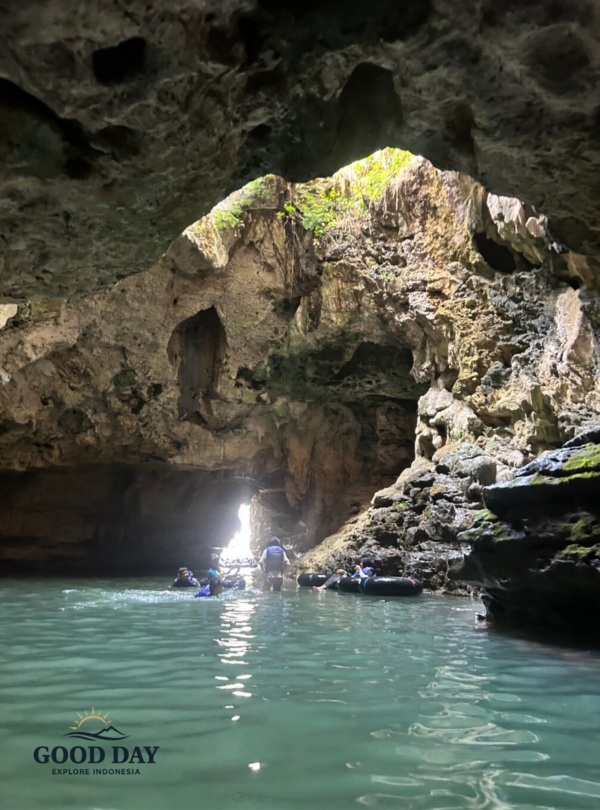 Visitors exploring the underground river inside Jomblang Cave in Yogyakarta, Indonesia, surrounded by towering limestone formations, crystal-clear water, and natural light entering through the cave opening.