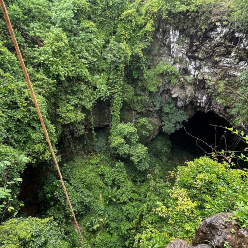 Aerial view of Jomblang Cave's giant sinkhole in Yogyakarta, Indonesia, surrounded by dense tropical vegetation, limestone cliffs, and the entrance to the famous underground cave system.