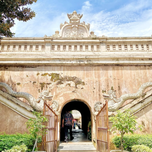 Historic entrance gate of Taman Sari Water Castle in Yogyakarta, Indonesia, featuring traditional Javanese architecture, dragon-shaped stairway ornaments, weathered palace walls, and visitors entering the royal heritage complex under a bright blue sky.