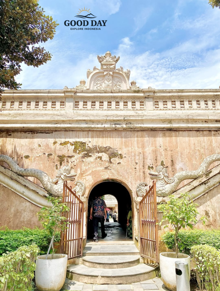 Historic entrance gate of Taman Sari Water Castle in Yogyakarta, Indonesia, featuring traditional Javanese architecture, dragon-shaped stairway ornaments, weathered palace walls, and visitors entering the royal heritage complex under a bright blue sky.