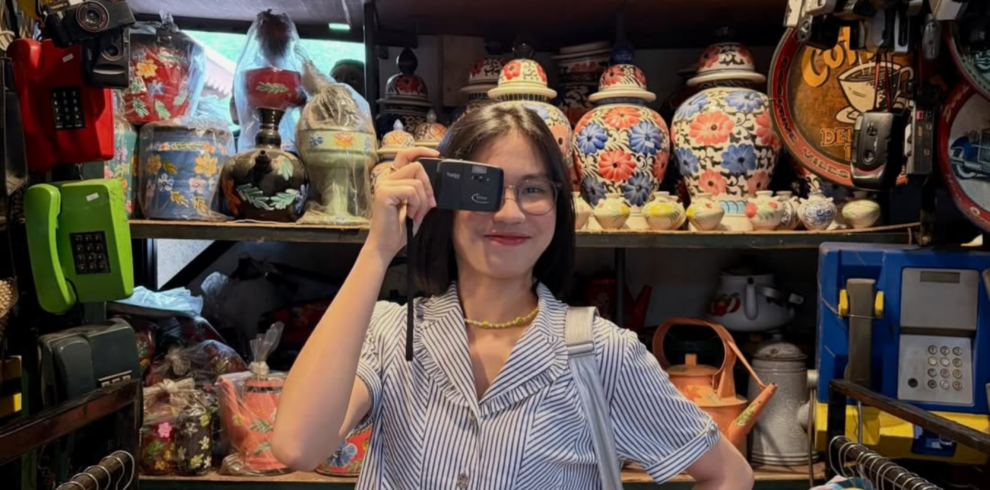 Visitor exploring a traditional market in Yogyakarta, Indonesia, standing among vintage collectibles, colorful batik clothing, antique fans, retro telephones, and classic decorative items inside a unique cultural souvenir shop.