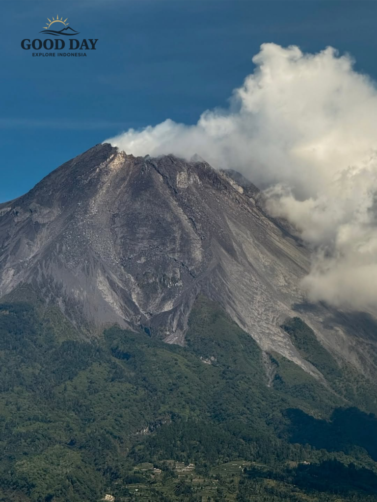 Close-up view of Mount Merapi volcano rising above the green landscapes of Yogyakarta, Indonesia, with dramatic volcanic slopes, rugged terrain, and clouds drifting around the summit.
