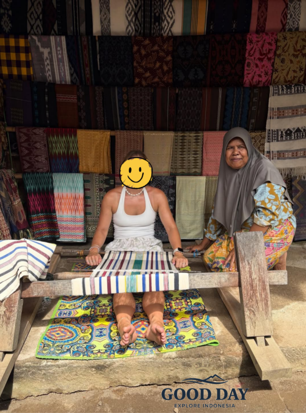 Visitor learning traditional Sasak weaving from a local artisan in Sade Traditional Village, Lombok, Indonesia, surrounded by colorful handwoven textiles and authentic cultural craftsmanship.
