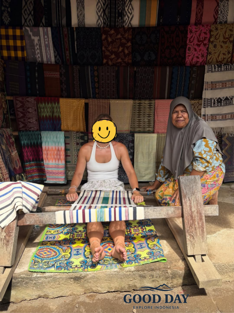 Visitor learning traditional Sasak weaving from a local artisan in Sade Traditional Village, Lombok, Indonesia, surrounded by colorful handwoven textiles and authentic cultural craftsmanship.