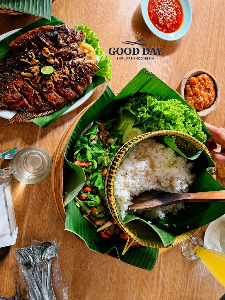 Traditional Sundanese food from Bandung served on banana leaves, featuring grilled fish, steamed rice in a woven basket, fresh vegetables, sambal, and local side dishes on a wooden dining table.