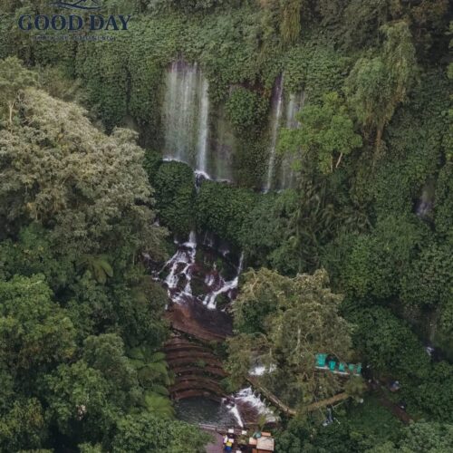 Aerial view of Benang Kelambu Waterfall in Lombok, Indonesia, surrounded by dense tropical rainforest, cascading streams, lush green cliffs, and natural pools hidden within the jungle