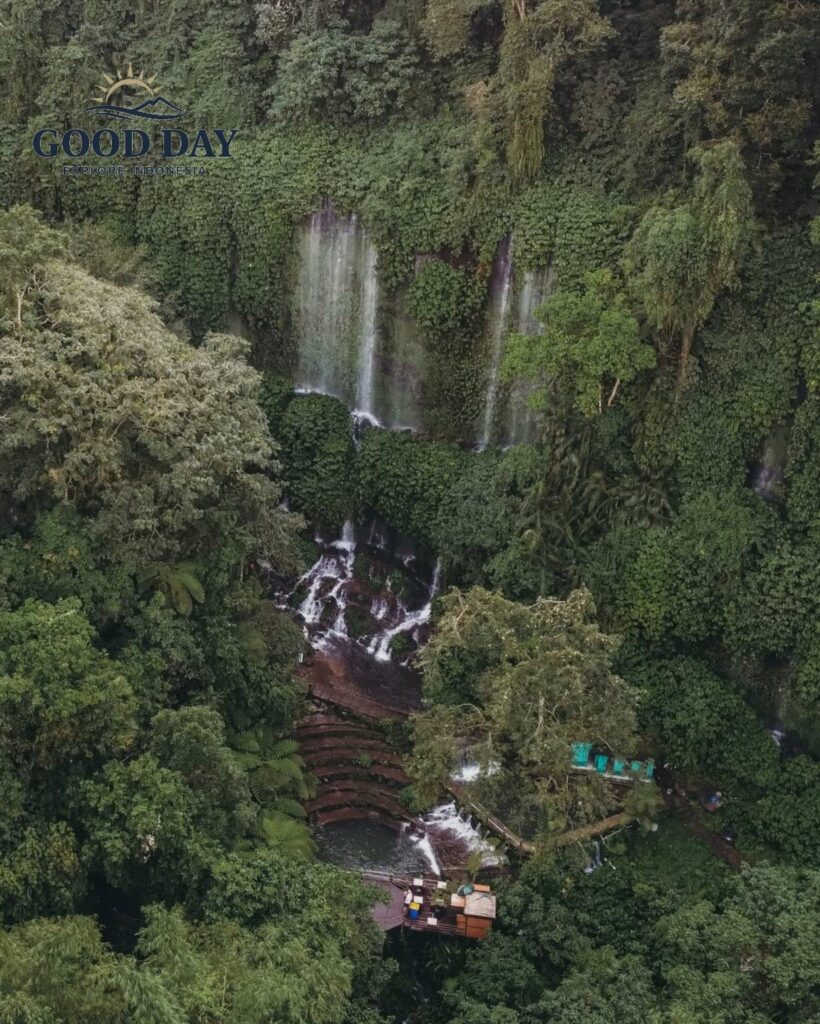 Aerial view of Benang Kelambu Waterfall in Lombok, Indonesia, surrounded by dense tropical rainforest, cascading streams, lush green cliffs, and natural pools hidden within the jungle