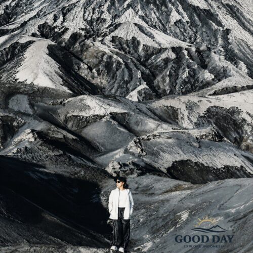 Traveler standing on the dramatic volcanic ash hills of Mount Bromo, surrounded by rugged black-and-white landscapes and unique sand formations in Bromo Tengger Semeru National Park, East Java, Indonesia.