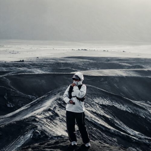 Traveler standing on the dramatic volcanic landscape of Mount Bromo, surrounded by black sand hills and rugged terrain in Bromo Tengger Semeru National Park, East Java, Indonesia.