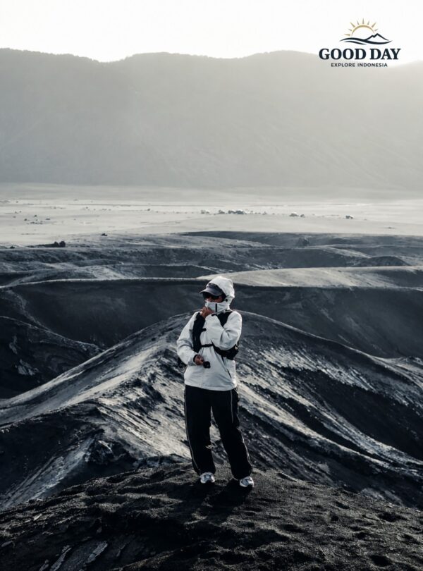 Traveler standing on the dramatic volcanic landscape of Mount Bromo, surrounded by black sand hills and rugged terrain in Bromo Tengger Semeru National Park, East Java, Indonesia.