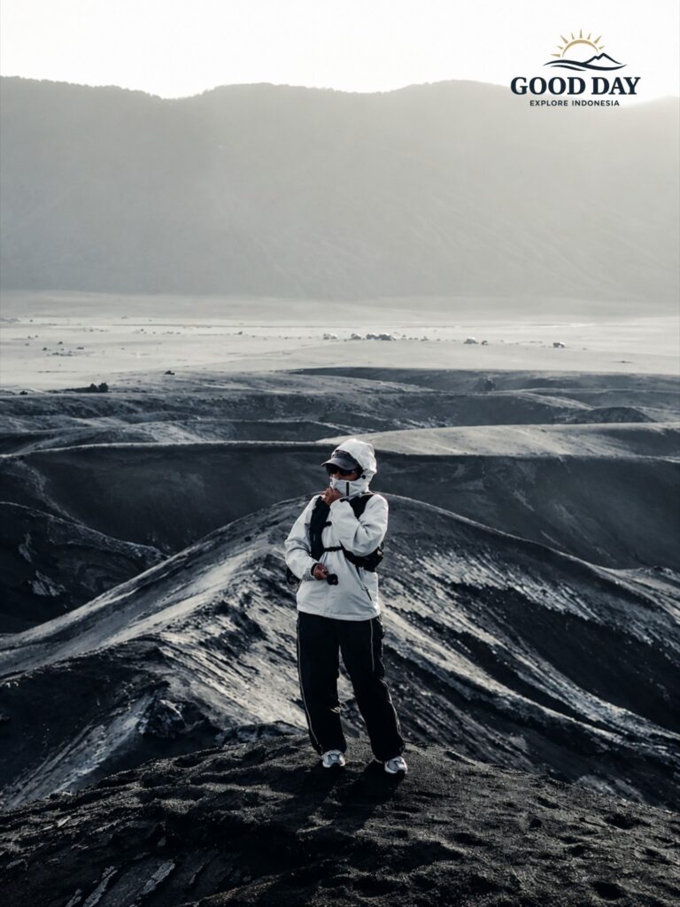 Traveler standing on the dramatic volcanic landscape of Mount Bromo, surrounded by black sand hills and rugged terrain in Bromo Tengger Semeru National Park, East Java, Indonesia.
