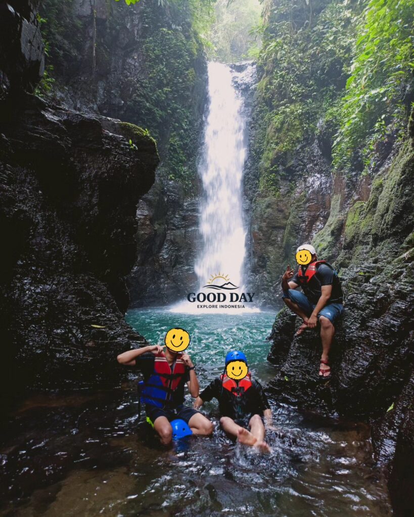 Visitors posing beside the stunning Curug Naga waterfall in Bogor, West Java, surrounded by towering canyon walls, crystal-clear water, and lush tropical rainforest during a body rafting adventure.