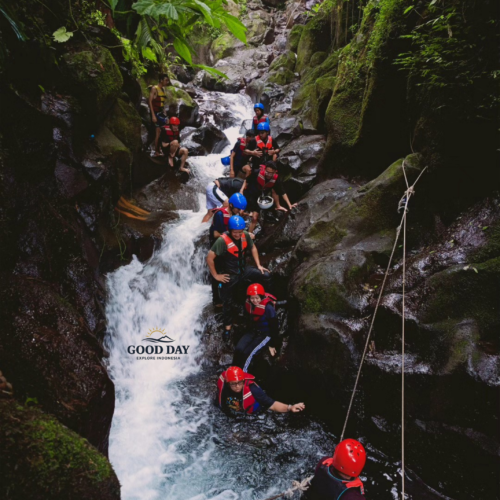 Participants navigating a rocky canyon during a body rafting adventure at Curug Naga, Bogor, wearing helmets and life jackets while trekking through waterfalls, natural pools, and lush tropical rainforest in West Java, Indonesia.