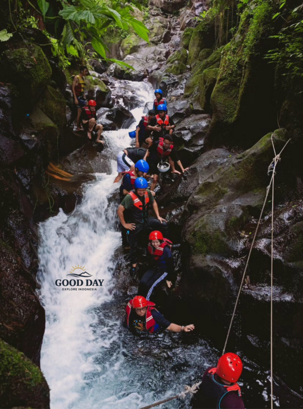 Participants navigating a rocky canyon during a body rafting adventure at Curug Naga, Bogor, wearing helmets and life jackets while trekking through waterfalls, natural pools, and lush tropical rainforest in West Java, Indonesia.