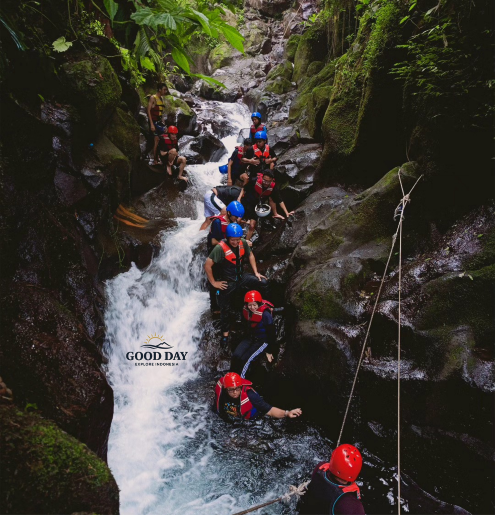 Participants navigating a rocky canyon during a body rafting adventure at Curug Naga, Bogor, wearing helmets and life jackets while trekking through waterfalls, natural pools, and lush tropical rainforest in West Java, Indonesia.