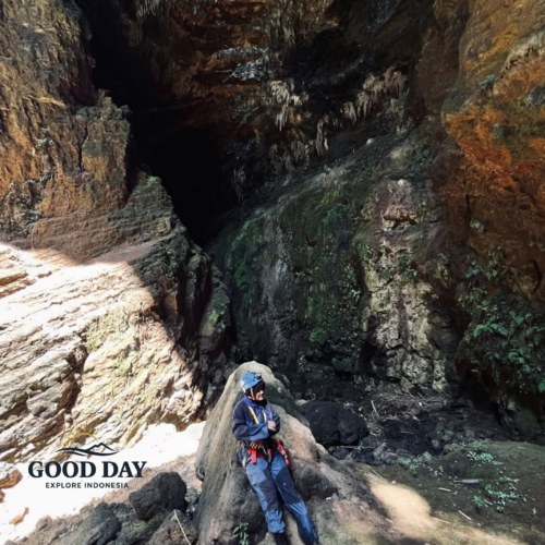 A cave explorer wearing safety gear rests on a large rock inside Goa Ngeleng, Yogyakarta, Indonesia. Surrounded by towering limestone walls, stalactites, and rugged cave formations, the scene highlights the raw beauty of this hidden underground destination in Gunungkidul.
