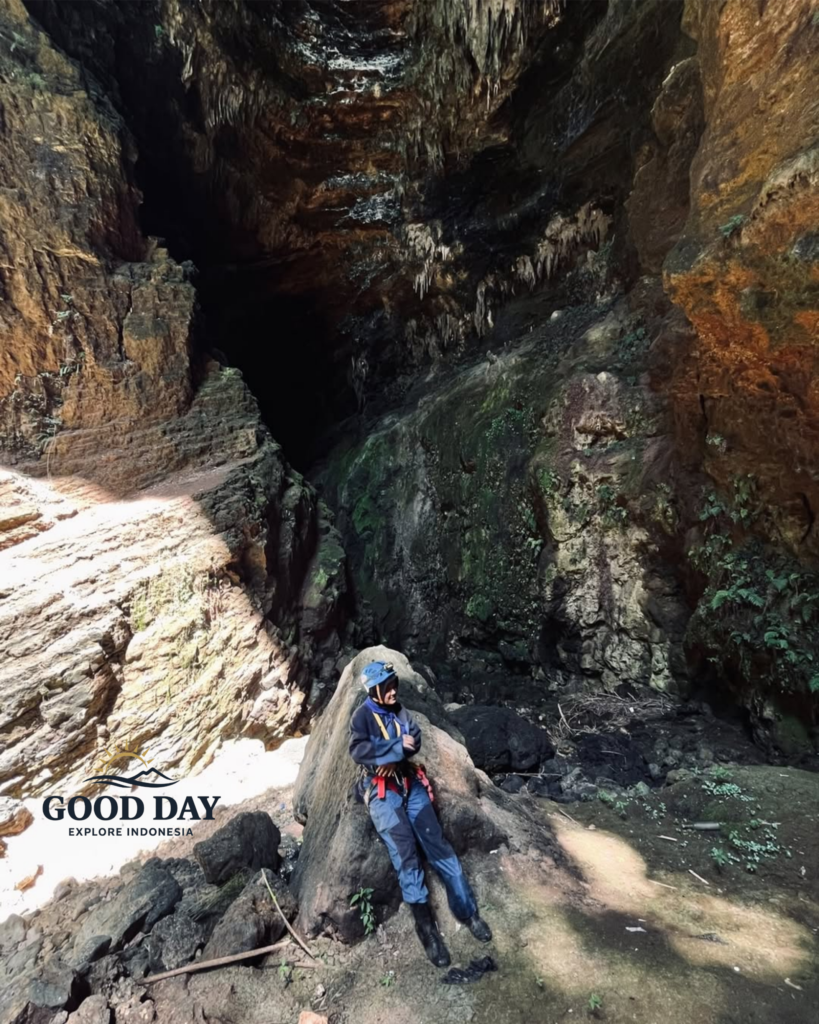 A cave explorer wearing safety gear rests on a large rock inside Goa Ngeleng, Yogyakarta, Indonesia. Surrounded by towering limestone walls, stalactites, and rugged cave formations, the scene highlights the raw beauty of this hidden underground destination in Gunungkidul.