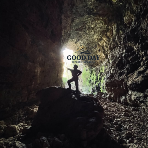 Silhouette of a cave explorer standing on a large rock inside Goa Ngeleng, Yogyakarta, Indonesia. Sunlight streams through the cave entrance, illuminating rugged limestone walls, rocky terrain, and the dramatic underground landscape of one of Gunungkidul's hidden natural attractions.