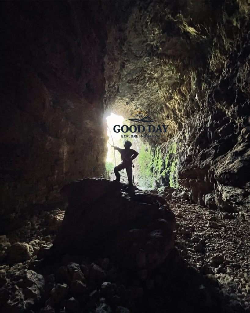Silhouette of a cave explorer standing on a large rock inside Goa Ngeleng, Yogyakarta, Indonesia. Sunlight streams through the cave entrance, illuminating rugged limestone walls, rocky terrain, and the dramatic underground landscape of one of Gunungkidul's hidden natural attractions.