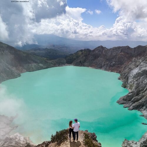 Couple standing on a cliff overlooking the turquoise crater lake of Kawah Ijen in Banyuwangi, East Java, Indonesia. The stunning volcanic landscape, crystal-blue acidic lake, and dramatic crater walls create one of the most breathtaking views in Indonesia.