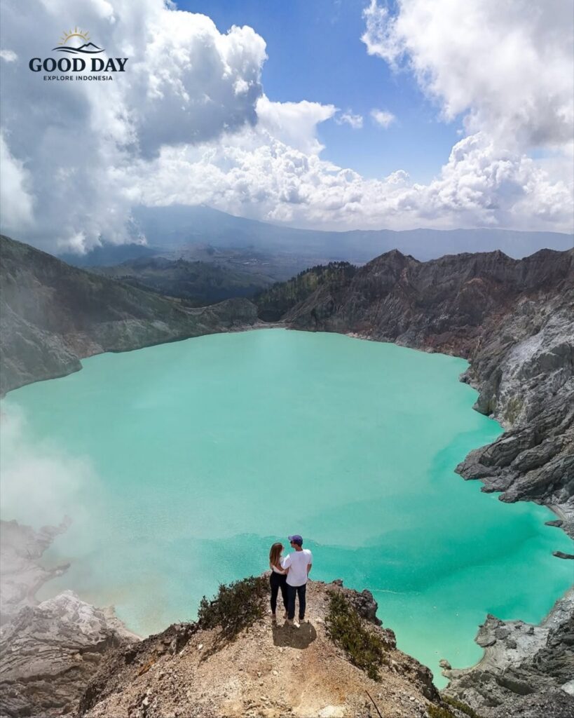 Couple standing on a cliff overlooking the turquoise crater lake of Kawah Ijen in Banyuwangi, East Java, Indonesia. The stunning volcanic landscape, crystal-blue acidic lake, and dramatic crater walls create one of the most breathtaking views in Indonesia.