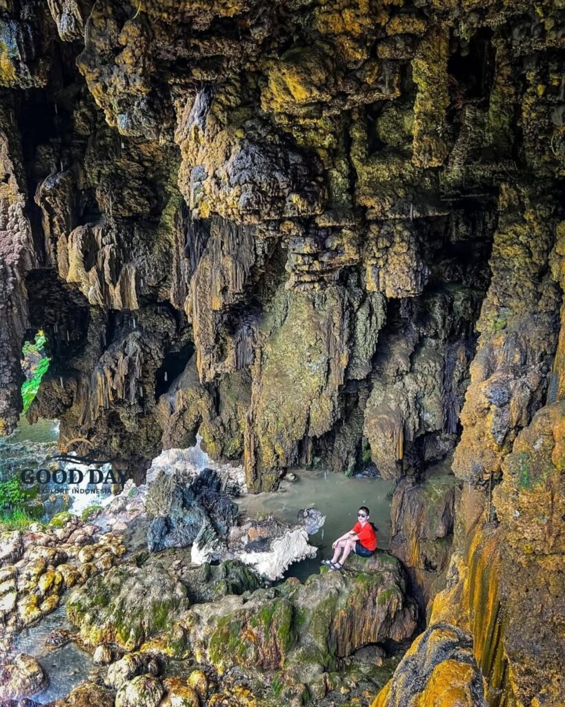 A traveler sitting on moss-covered rocks inside Goa Tetes in Lumajang, East Java, surrounded by massive limestone formations, natural cave walls, flowing spring water, and unique stalactite-like rock textures.