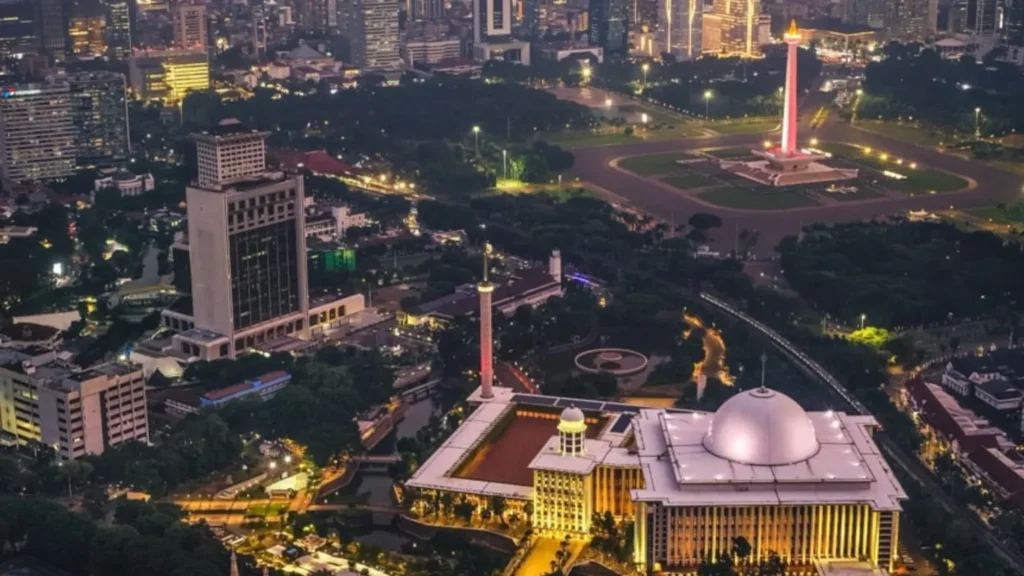 Drone aerial view of Istiqlal Mosque and the National Monument (Monas) in Central Jakarta, Indonesia, illuminated at night.
